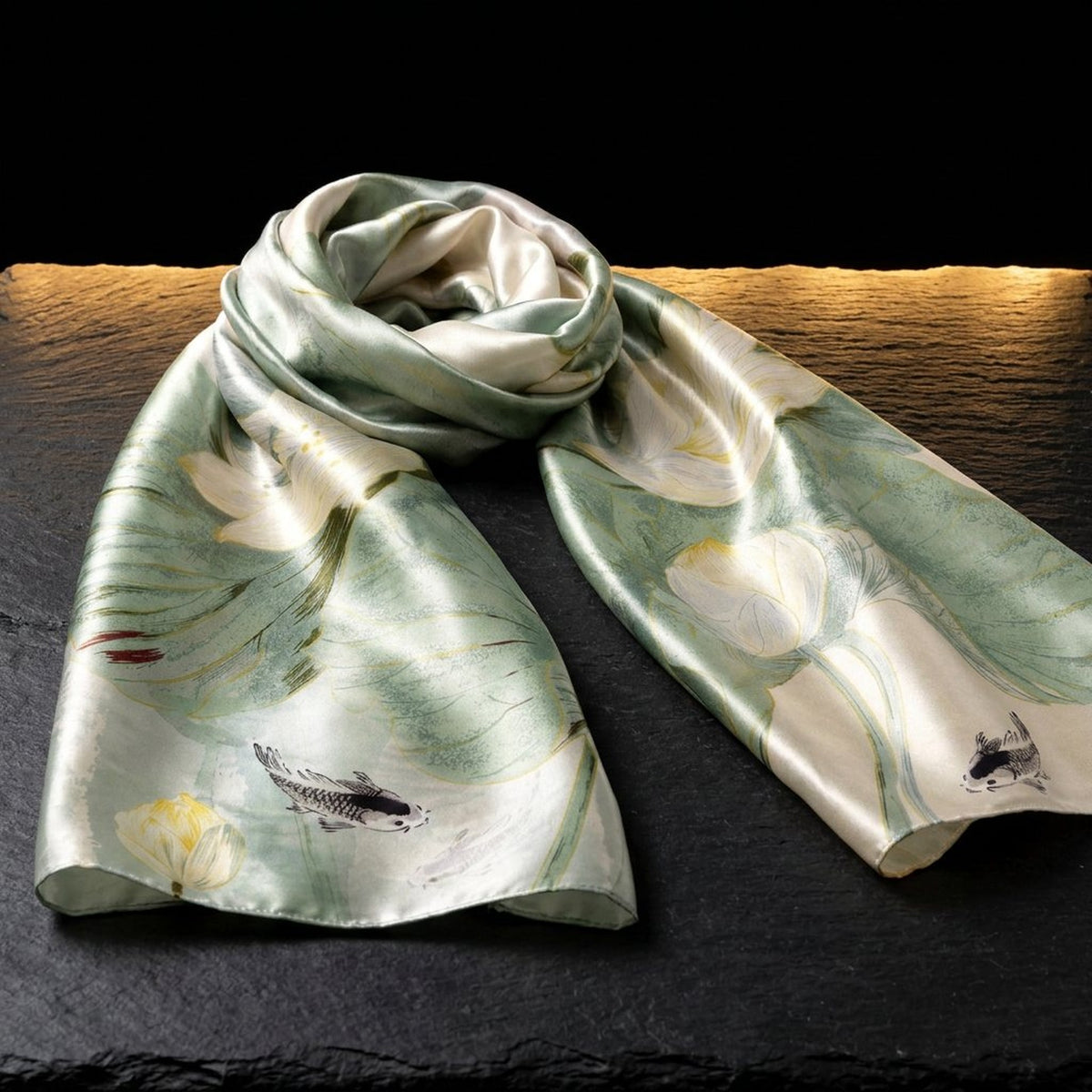 Lotus Breeze sage green silk scarf for women with a pale lotus flower print, laid on dark slate