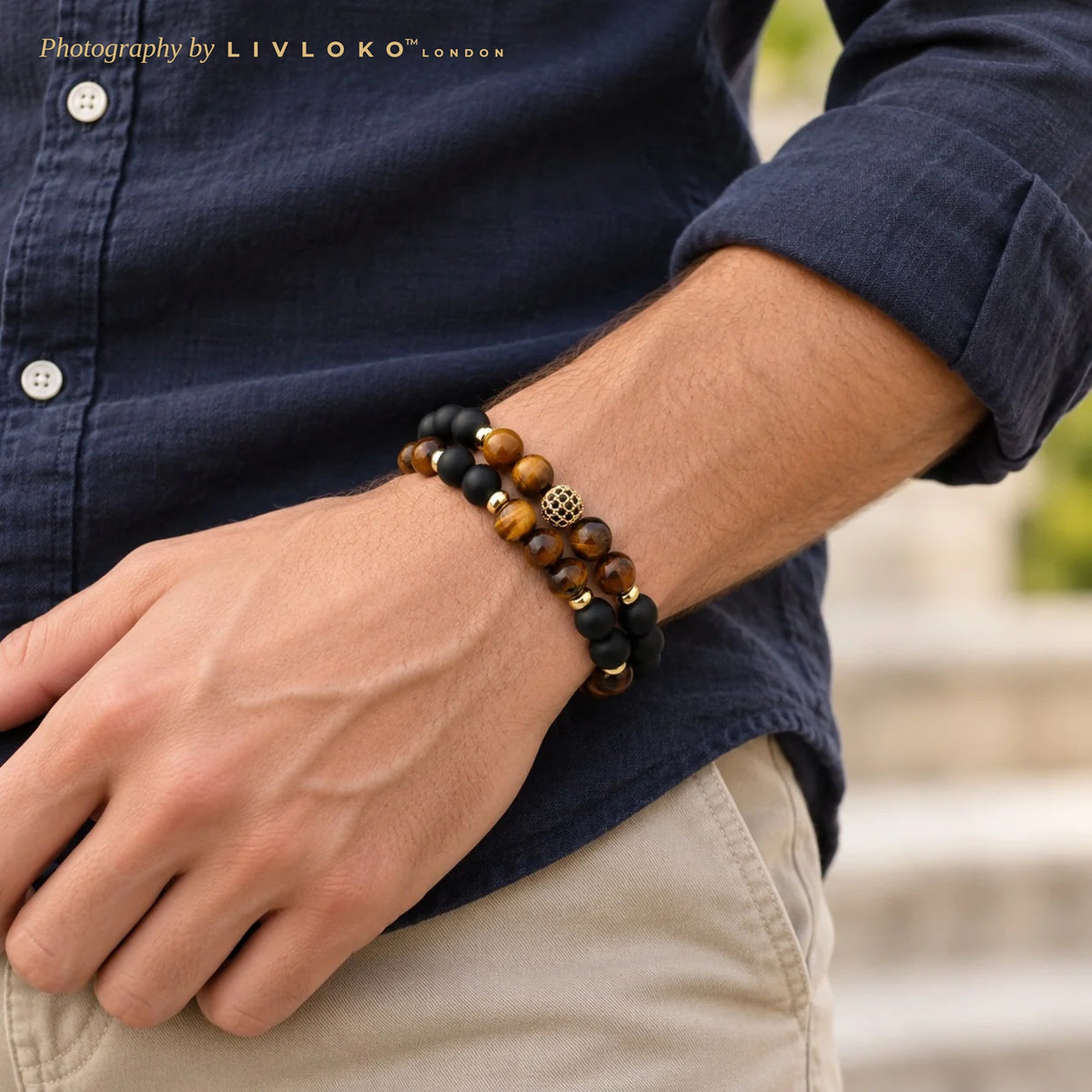 Men's tiger eye and black agate bracelet set with gold pavé ball worn on the wrist with a navy linen shirt