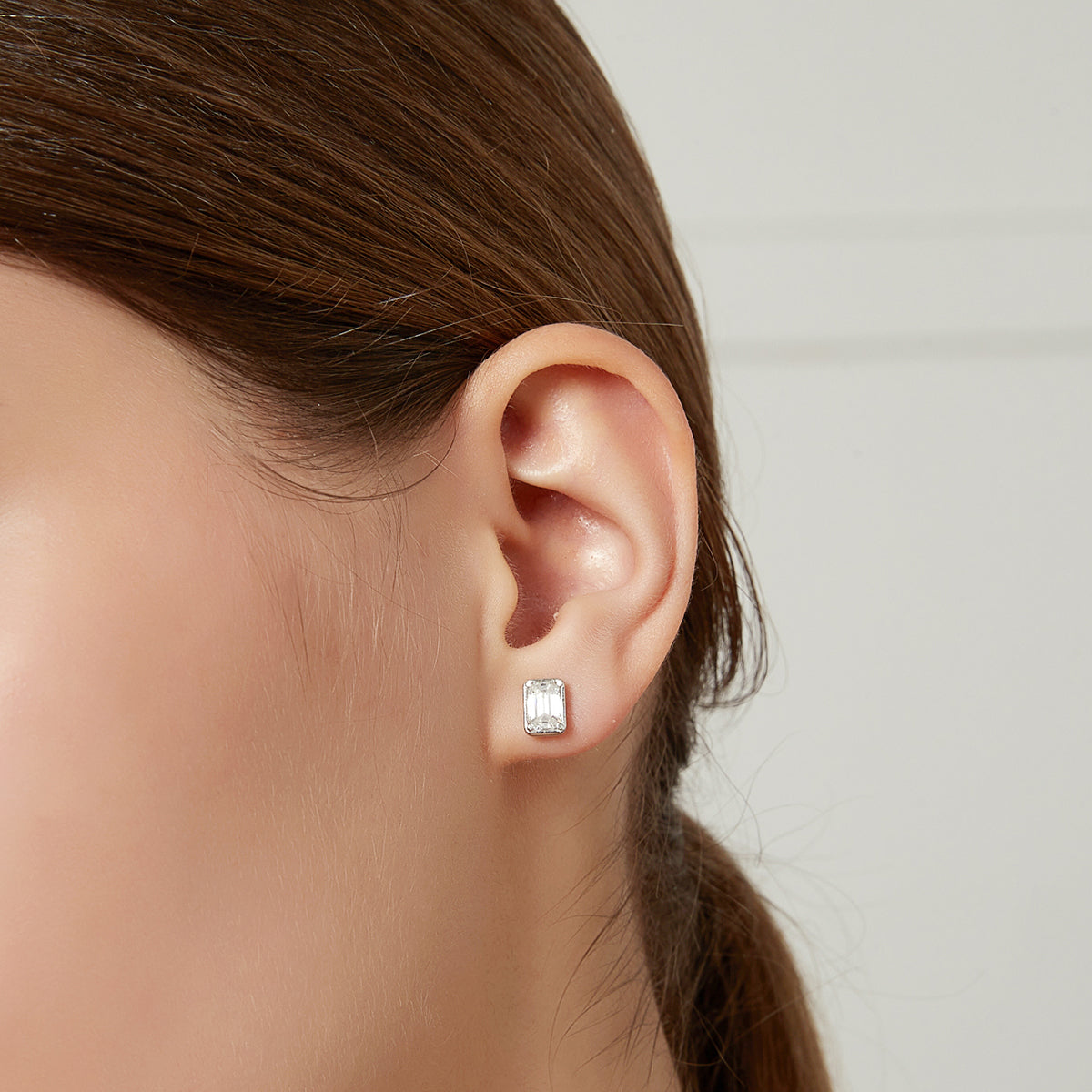 Side profile of a woman with her hair tied back wearing a small rectangular stud earring