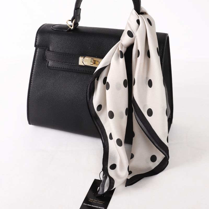 Ivory scarf with black polka dots tied to the handle of a black top-handle handbag