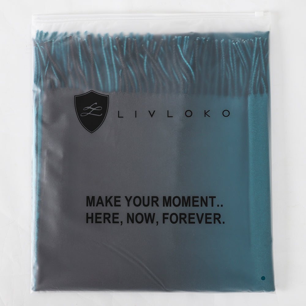 Folded teal and black shawl inside a translucent LIVLOKO bag printed Make your moment, here, now, forever