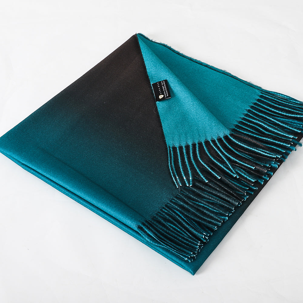 Shawl folded with one corner turned back, showing the teal and black sides, a sewn label and fringe