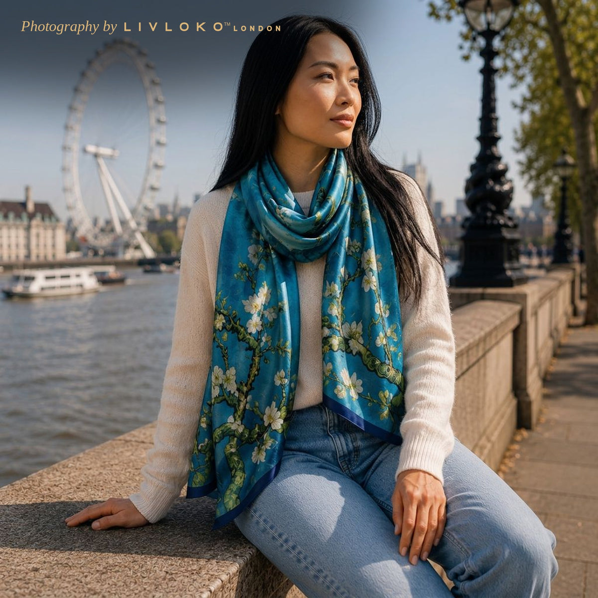 Woman wearing the Azure Blossom blue floral mulberry silk scarf looped at the neck by the Thames in London