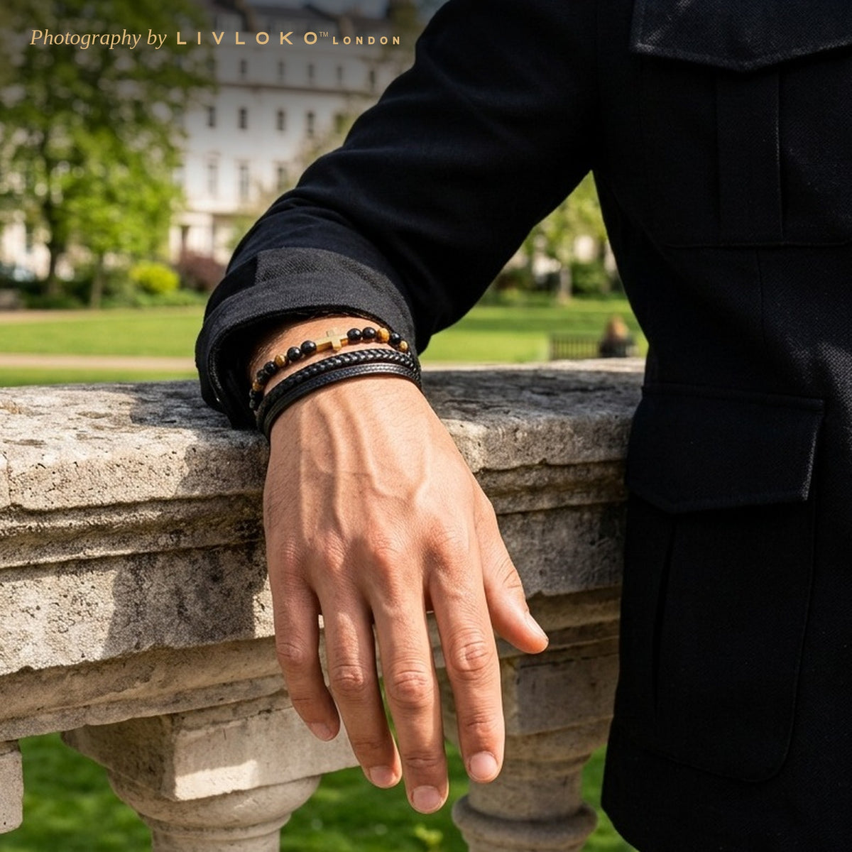 Man wearing the men's black leather bracelet with gold cross and tiger eye beads in a London park