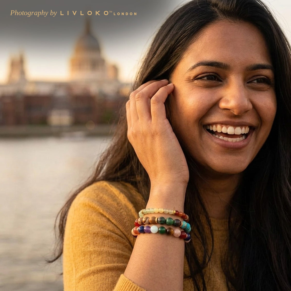 Woman wearing the Livloko London gold plated 7 chakra bracelet set stacked on her wrist by the Thames in London
