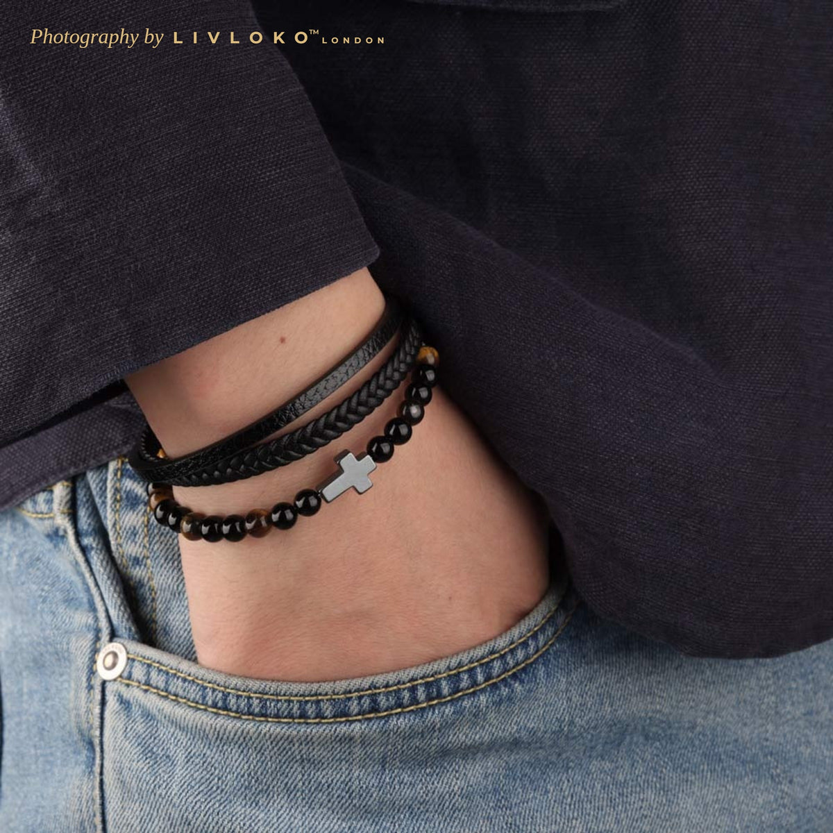 Men's black leather cross bracelet with tiger eye beads worn on the wrist, hand in jeans pocket