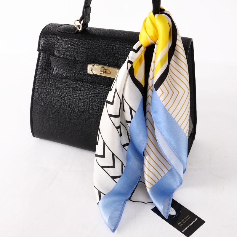 Geometric scarf tied to the handle of a black handbag, showing chevron, stripe and pale blue border
