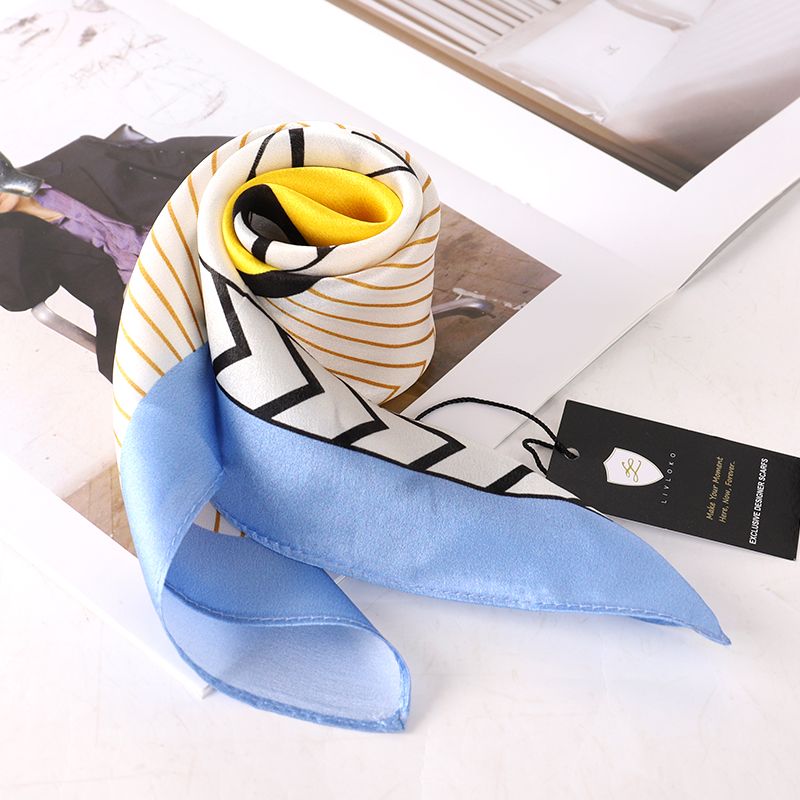 Scarf folded and rolled on an open magazine with its pale blue edge spread out and a black swing tag